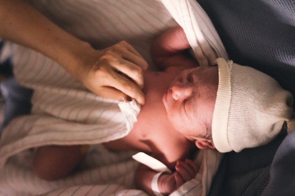 A serene moment of a newborn baby swaddled in blankets with a tender touch of a parent's hand.
